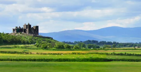 Tipperary's famous Rock of Cashel is seen surrounded by green fields and mountains in the distance.