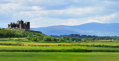 Tipperary's famous Rock of Cashel is seen surrounded by green fields and mountains in the distance.
