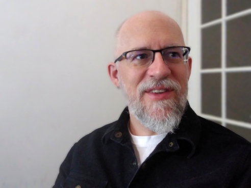 A headshot of Christopher Torgalson. He is wearing black spectacles and is standing next to a window.