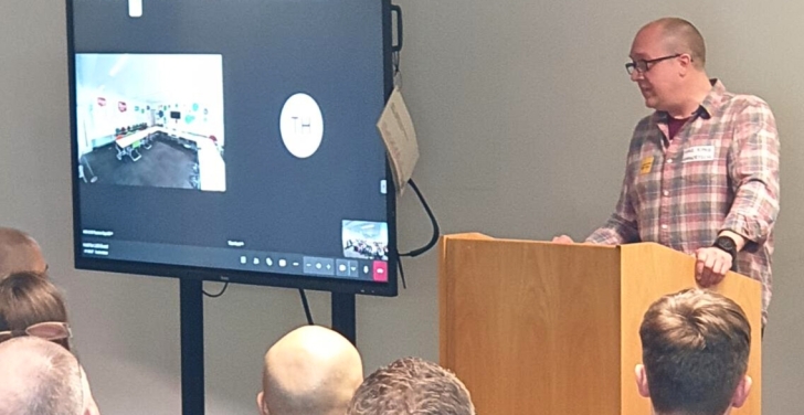 Mike King is behind a podium, delivering a presentation at LocalGov Drupal Camp in Birmingham.