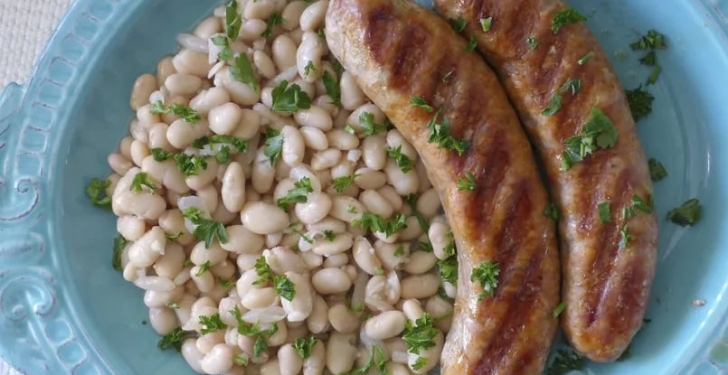 White beans on a plate with two sausages next to them.