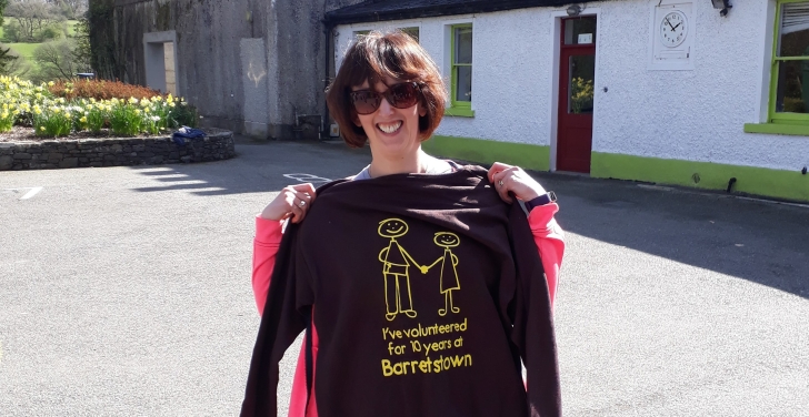 Claire O'Brien holds up a brown and yellow hoodie that says “I've volunteered for 10 years at Barretstown.“