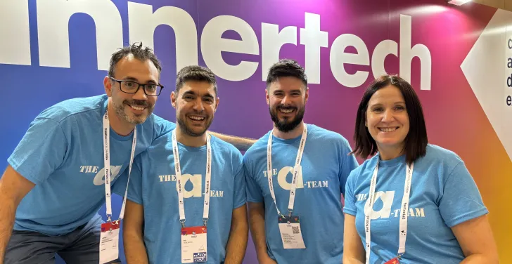 Four Annertech staff members in blue T-shirts that say “The A-Team“ sit in front of the Annertech booth.