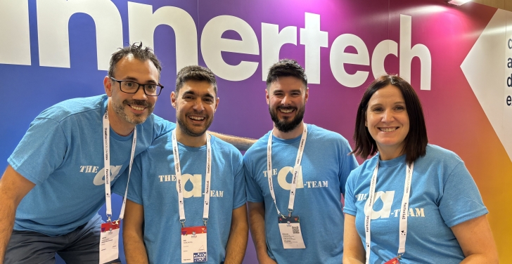 Four Annertech staff members in blue T-shirts that say “The A-Team“ sit in front of the Annertech booth.