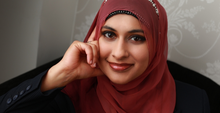Fatima Mahmood rests her face on her hand. She is dressed in black with a red headscarf.