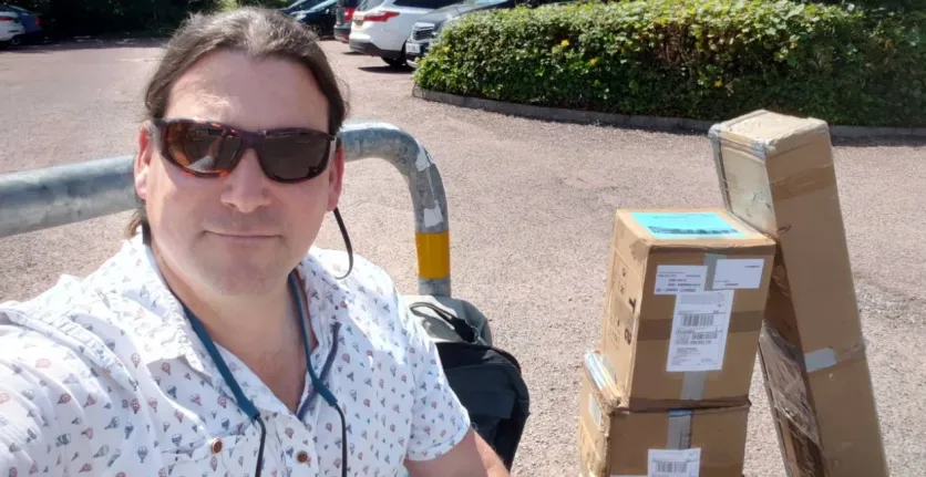 Annertech's Simon White takes a selfie with three boxes filled with banners and swag.