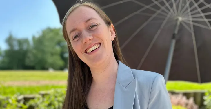 Fiona Spellman stands outside in the sunshine under an umbrella. 