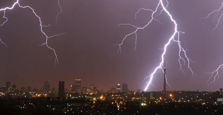Huge flashes of lightning streak across the sky, over a cityscape of Johannesburg.