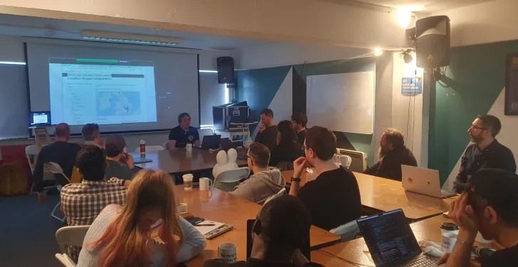 A room of people at desks, listening to a presentation