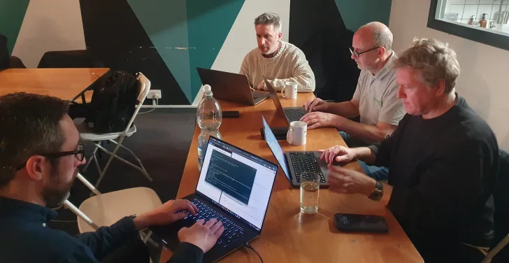 Four people sit at a table with laptops