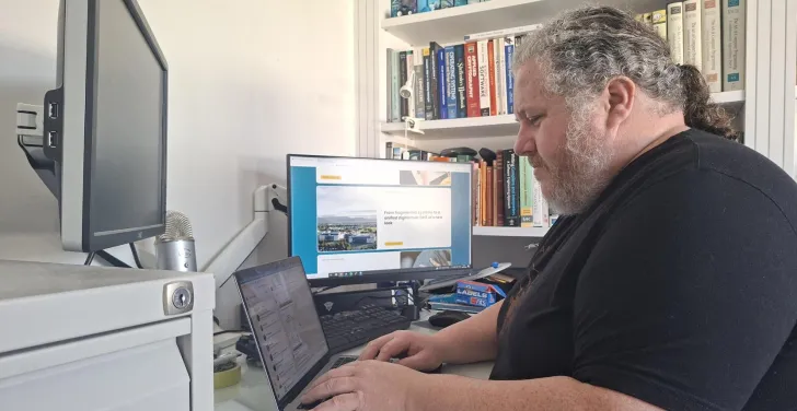 Dermot at his desk typing on a laptop.