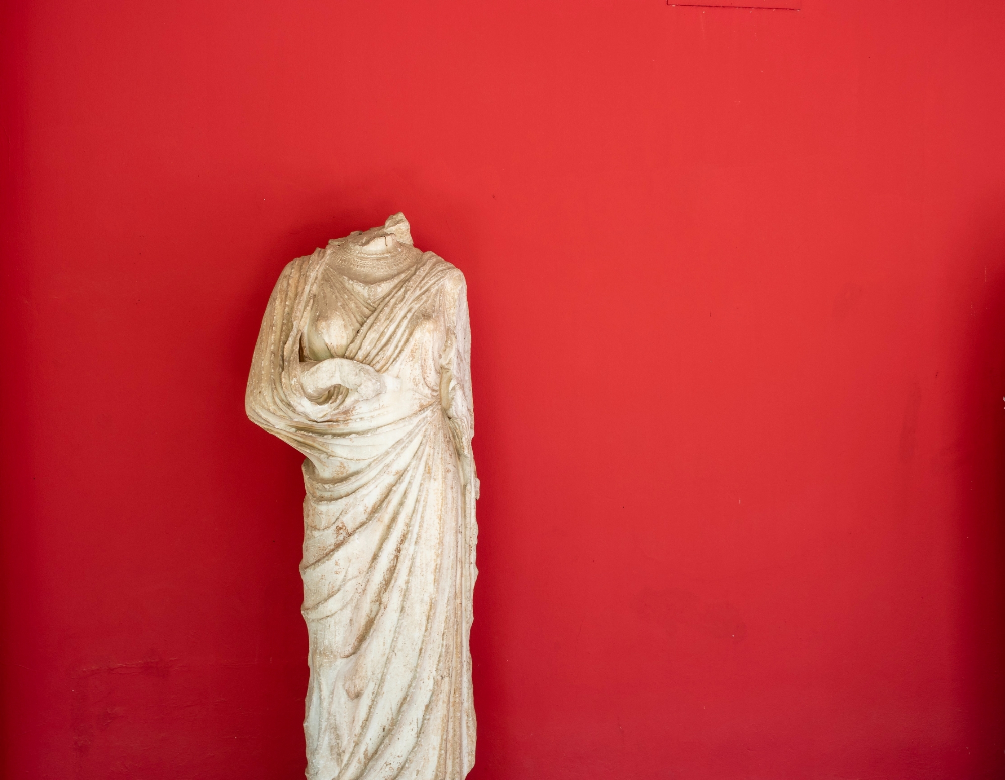 Statue with head missing, against red background - from unsplash.