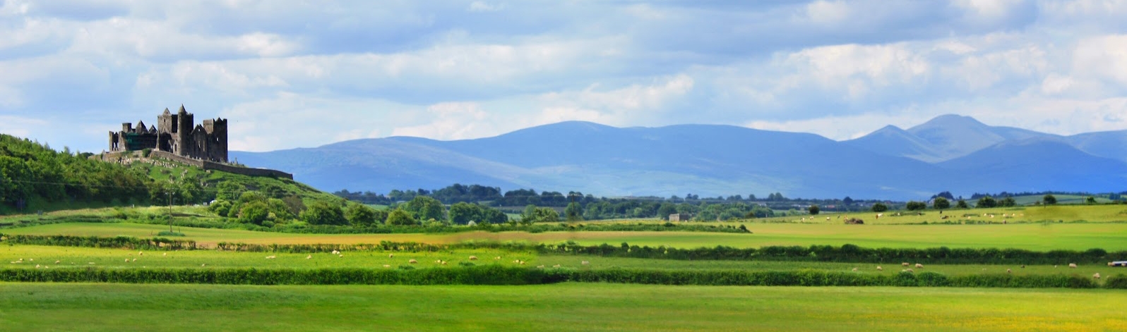 Tipperary's famous Rock of Cashel is seen surrounded by green fields and mountains in the distance.