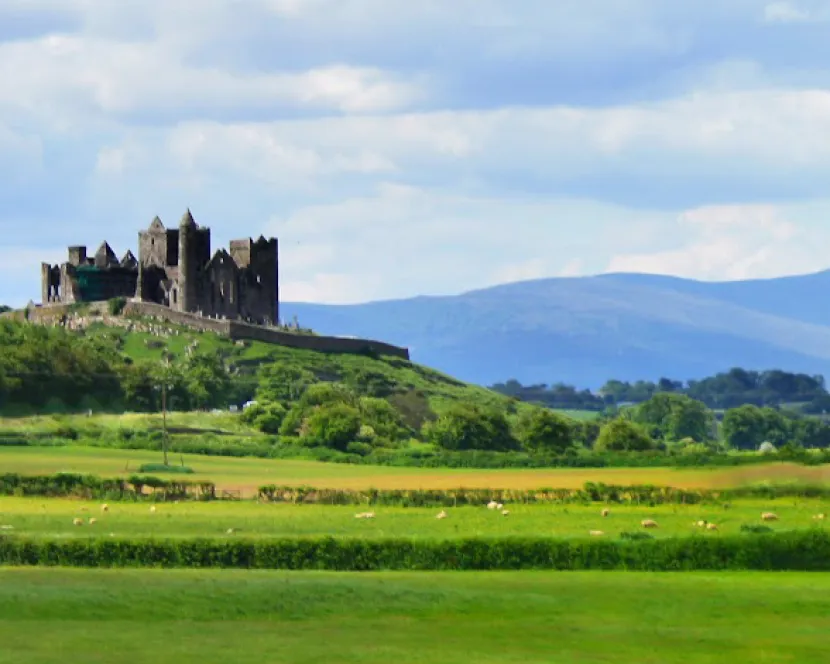 Tipperary's famous Rock of Cashel is seen surrounded by green fields and mountains in the distance.