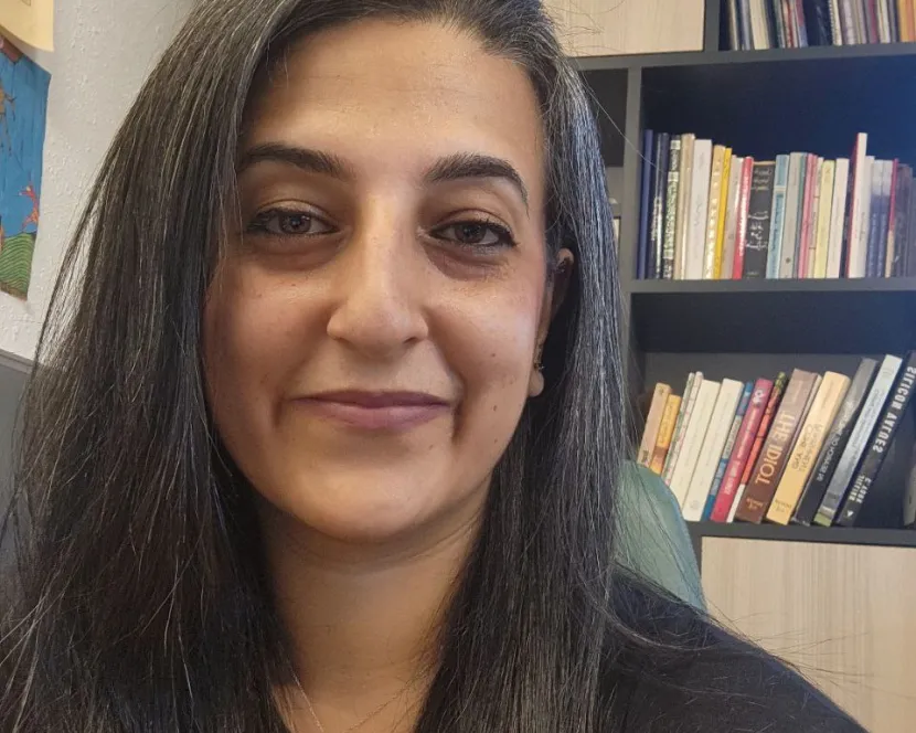 Layal Khatib sits in her office. Behind her is a bookshelf brimming wiht books.