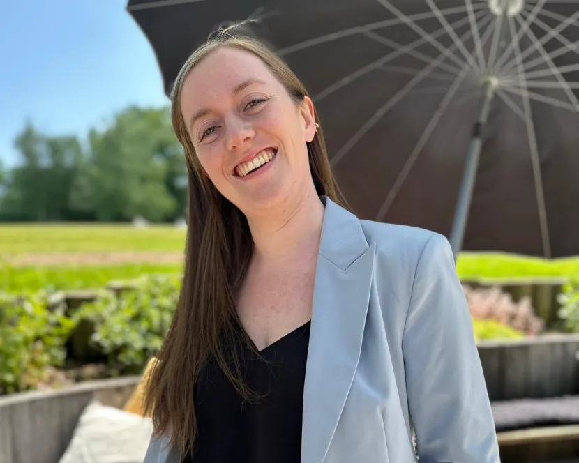 Fiona Spellman stands outside in the sunshine under an umbrella. 