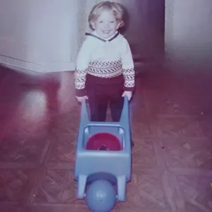 A young Alan Burke pushes a wooden wheelbarrow.