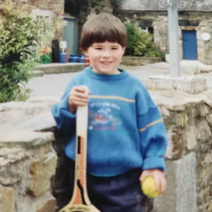 A young Sean O'Connell holds a wooden tennis racket and a ball.