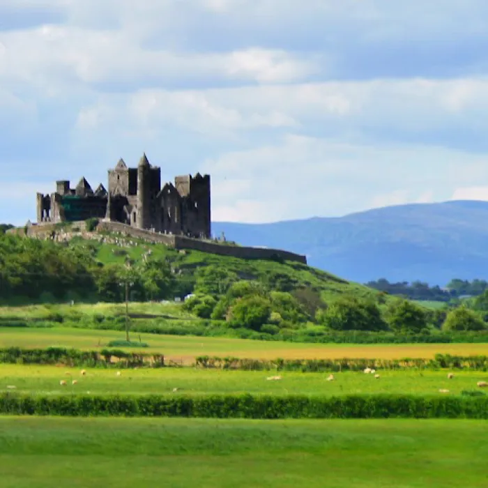 Tipperary's famous Rock of Cashel is seen surrounded by green fields and mountains in the distance.