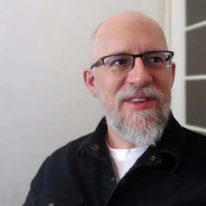A headshot of Christopher Torgalson. He is wearing black spectacles and is standing next to a window.