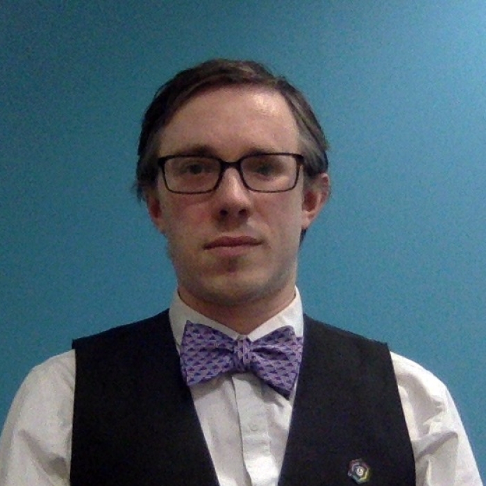 John Cook in a very smart suit, with waistcoast and a purple bowtie.