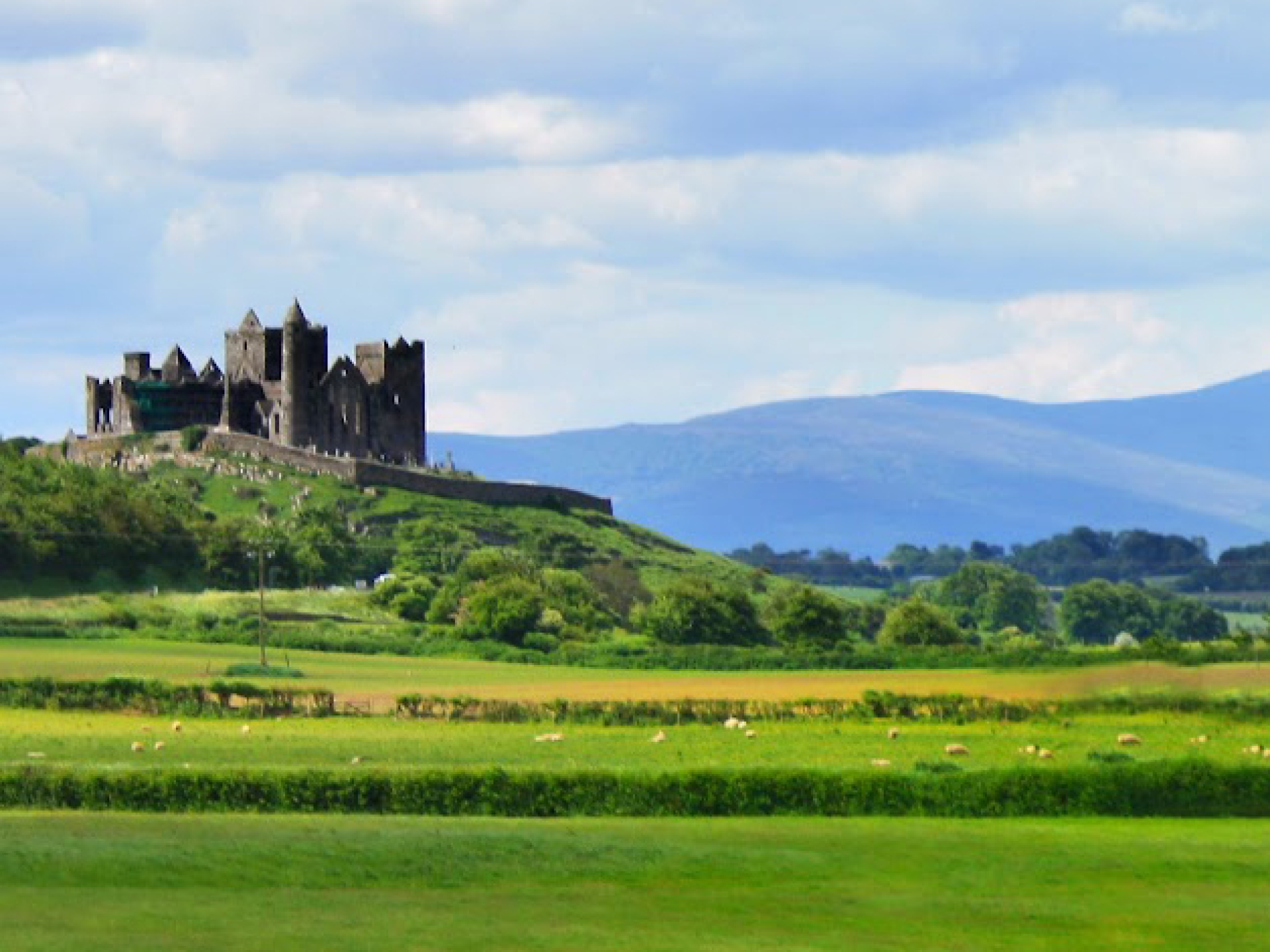 Tipperary's famous Rock of Cashel is seen surrounded by green fields and mountains in the distance.