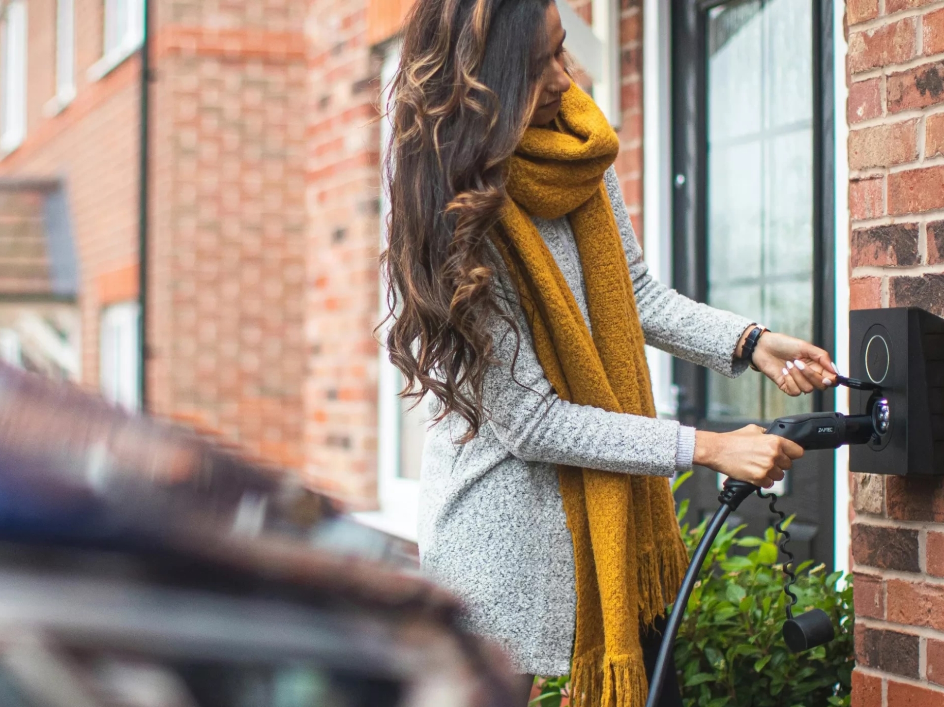 A woman plugs in the charging cable for her electric vehicle.