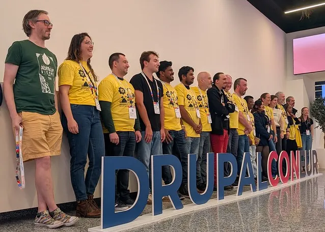 A group of people stand behind the DrupalCon Eur sign.